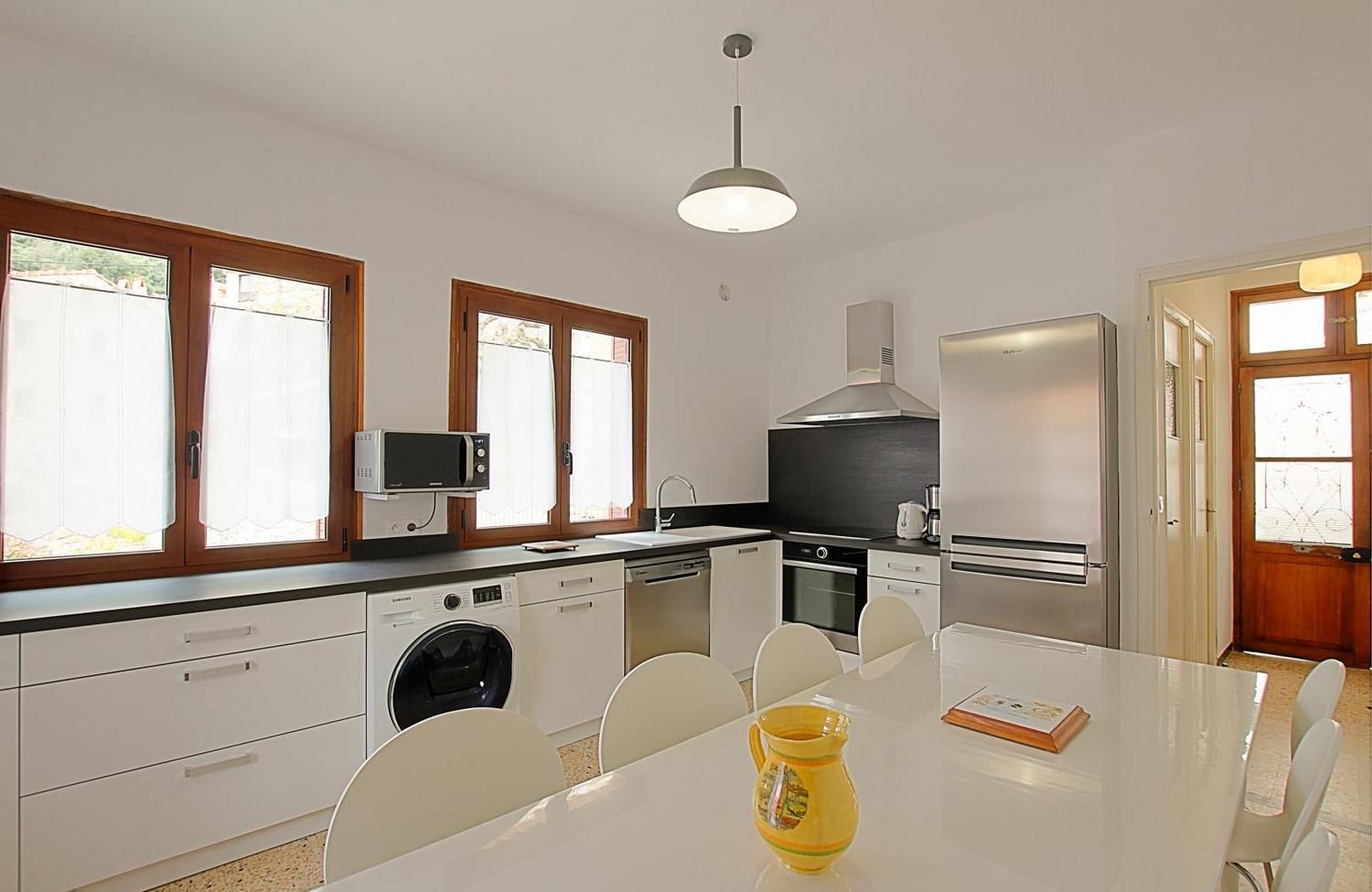 A modern kitchen with a built-in washing machine, a microwave, and a stove. There is a dining table with chairs and a yellow pitcher on it.