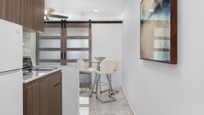 A modern kitchen with wooden cabinets, a glass-top table, and two white chairs. - JR ONE BR ESJ TOWERS! HIGH FLOOR,VIEW LOCATION! (Carolina)