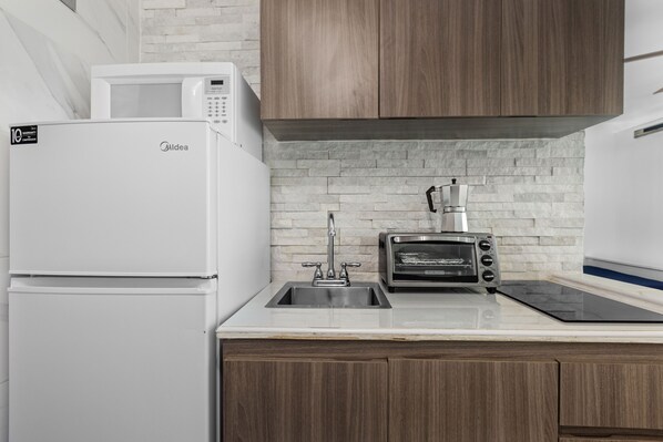 A kitchen with a white refrigerator, a microwave, a toaster oven, and a sink.