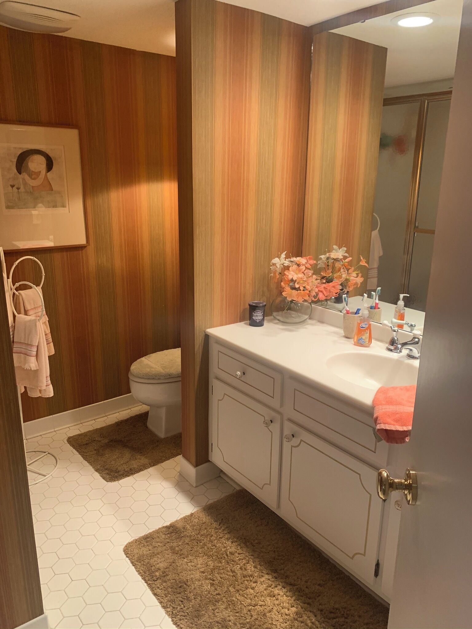 A bathroom with a white sink, a mirror, a toilet, and a shower. There are towels hanging on a rack and a rug on the floor.