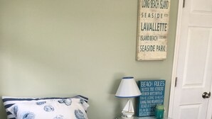 A bedroom with a bed featuring a seashell pattern bedspread, a nightstand with a lamp, and a sign listing beach rules. - Cottage located 1 block from the beach and 1 block to the bay in Ocean Beach 2 (Lavallette)
