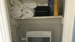 A compact laundry room with a front-loading washing machine, a dryer, and a shelf above containing folded towels and cleaning supplies. - Cottage located 1 block from the beach and 1 block to the bay in Ocean Beach 2 (Lavallette)