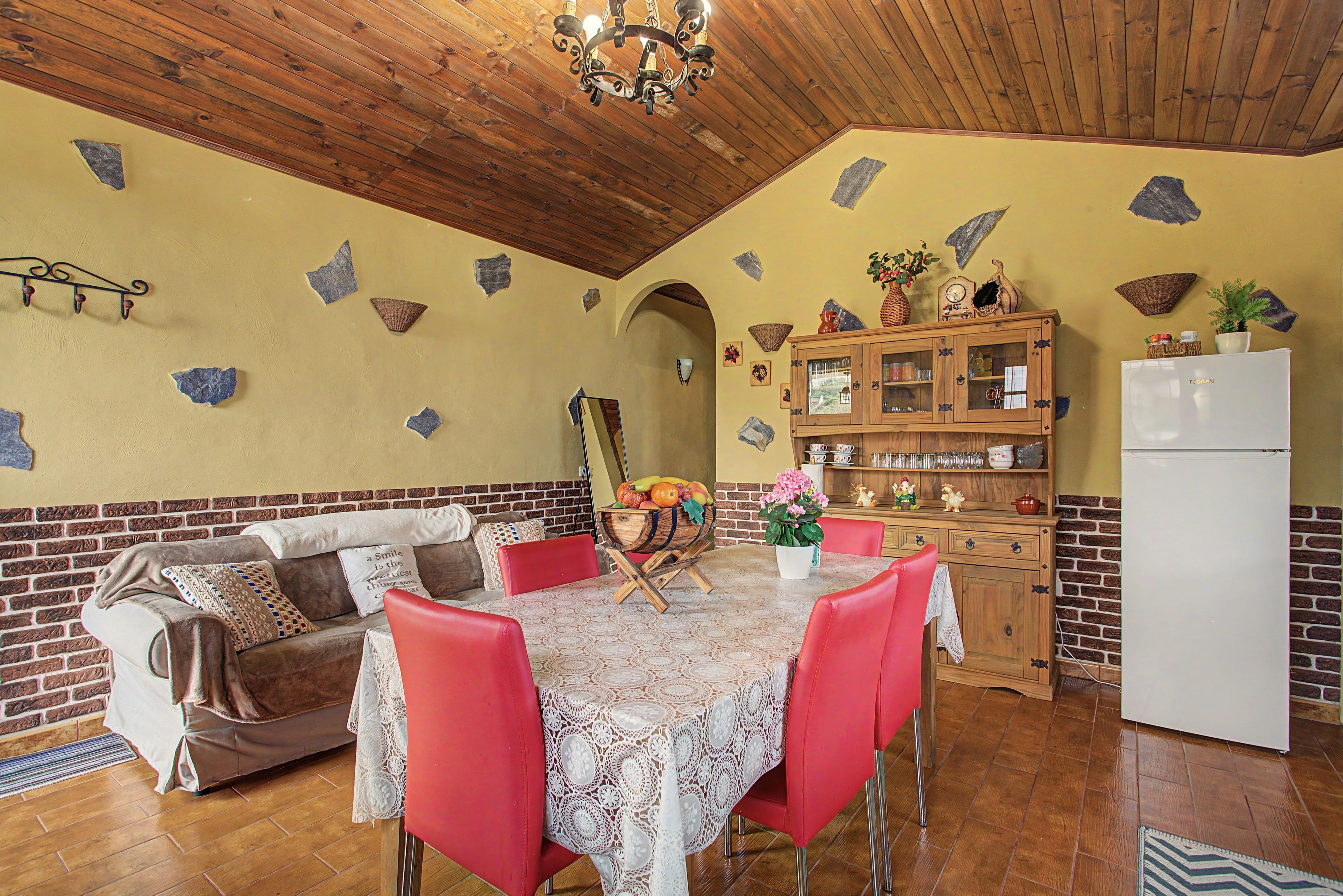 Una cocina acogedora con techo de madera, una mesa de comedor con sillas rojas, una pared de ladrillo y un refrigerador blanco.