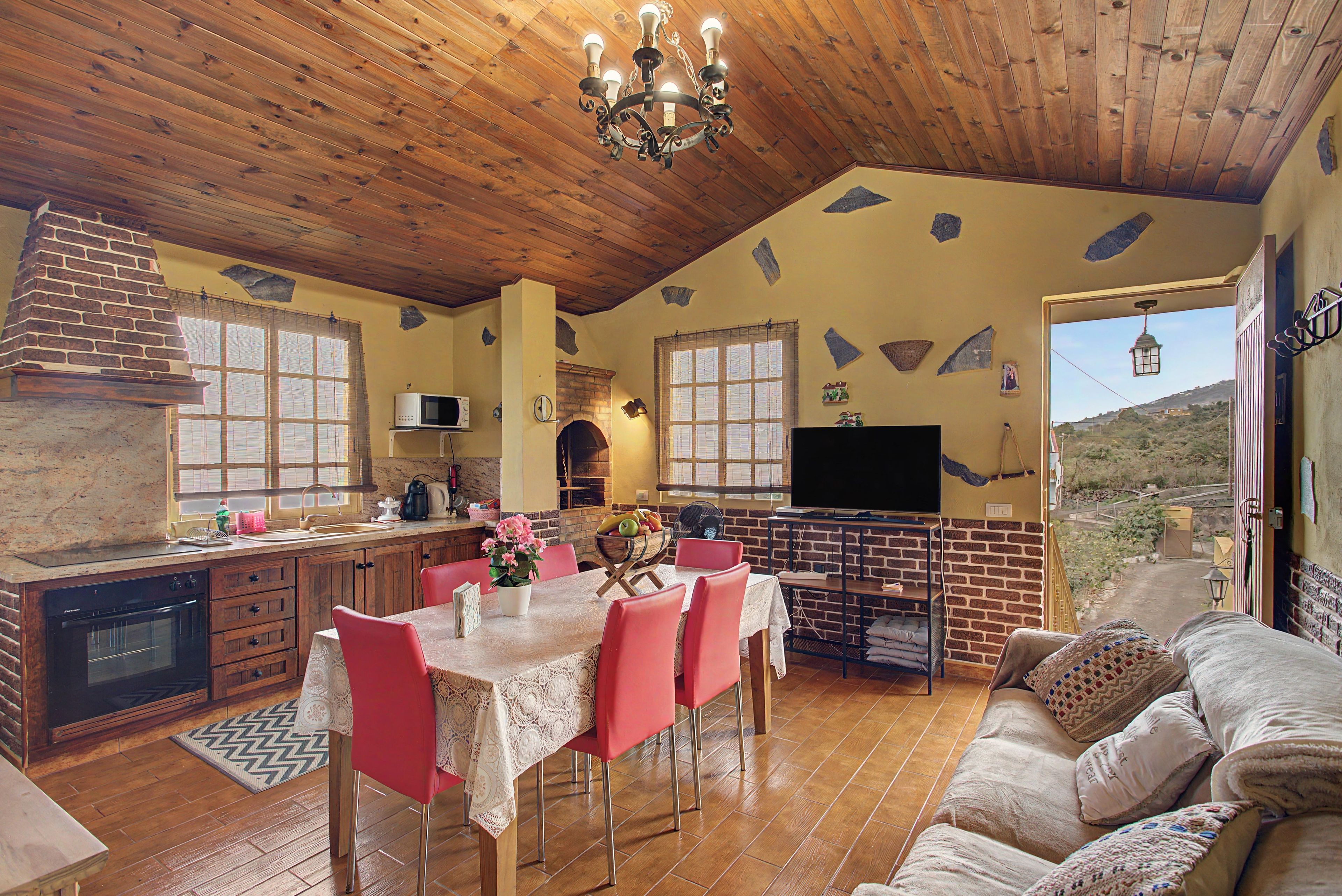 Un amplio espacio de sala con una mesa de comedor, sillas rojas, un sofá, una chimenea y un televisor.