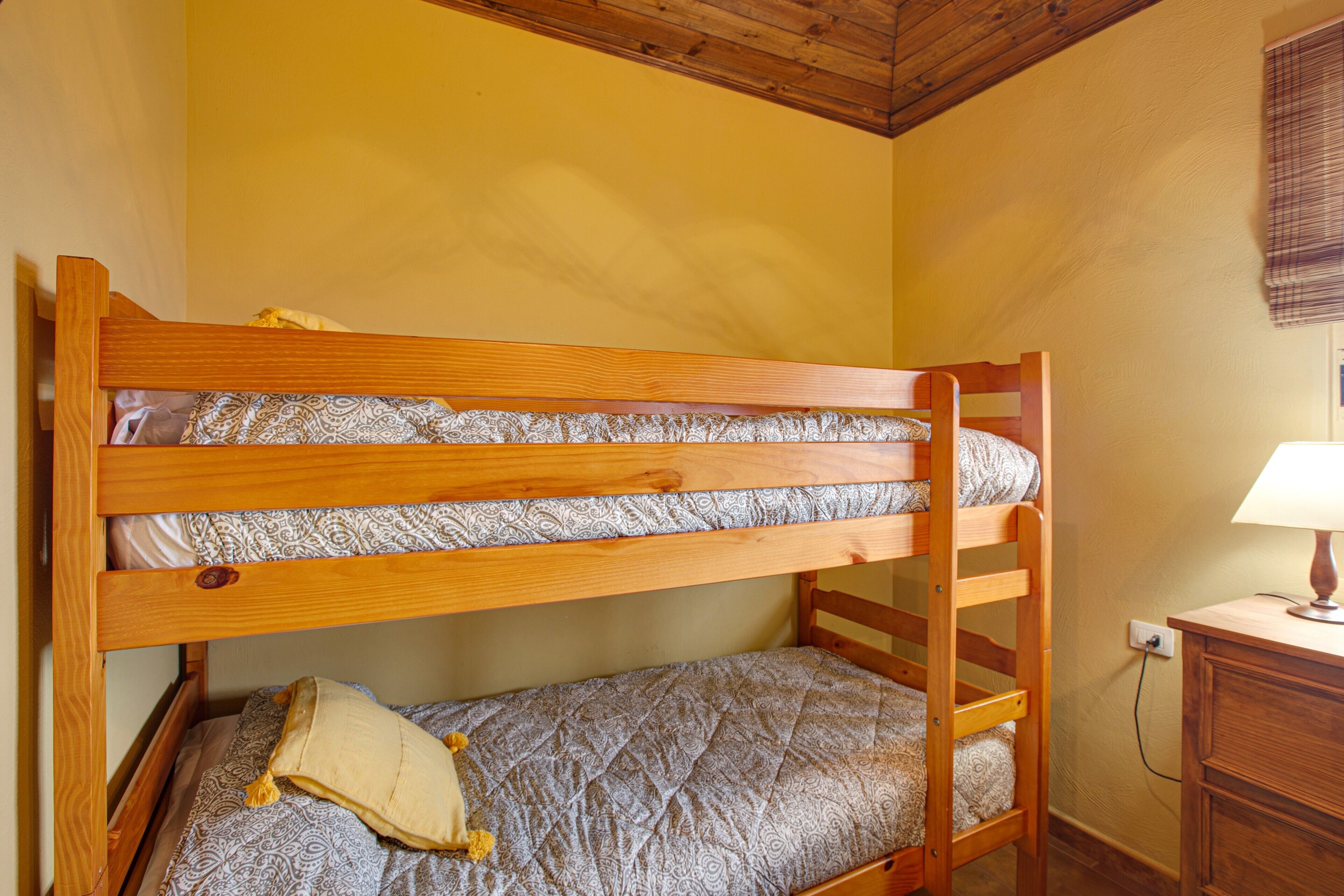A bunk bed with patterned bedding, a wooden headboard, and a bedside table with a lamp.