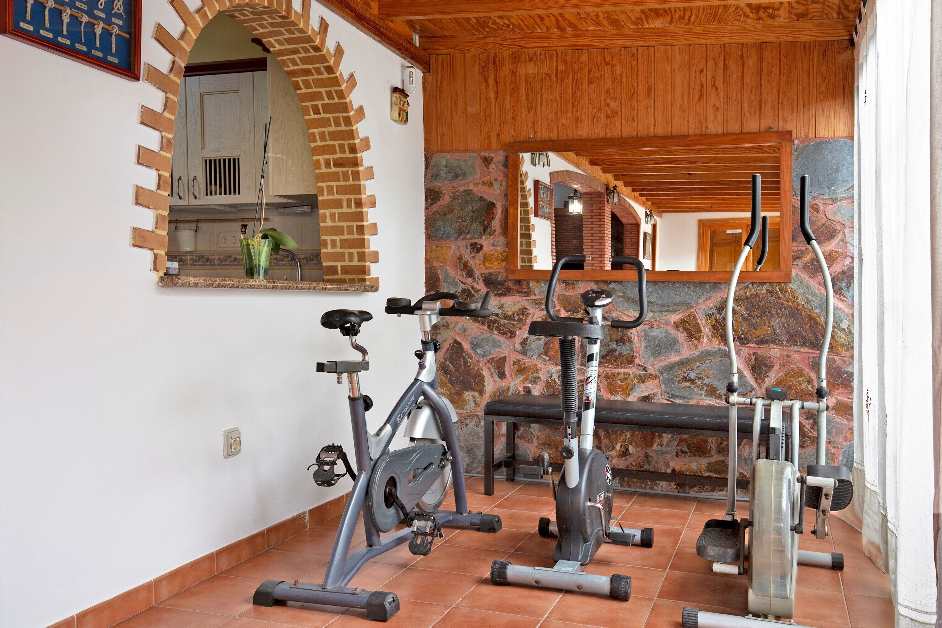 Un gimnasio con equipo de ejercicio, pared de piedra y techo de madera.