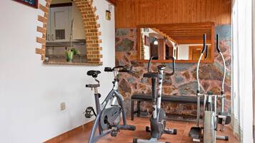 Un gimnasio con equipo de ejercicio, pared de piedra y techo de madera.
