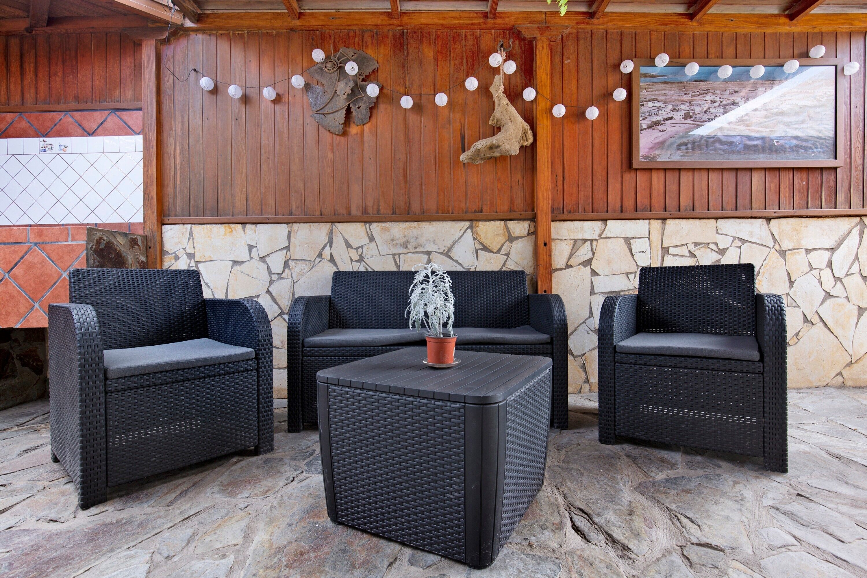 A covered patio area with wicker furniture, a stone floor, wooden walls, and a mounted picture.