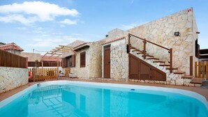 Une piscine avec des murs en pierre et des rampes en bois, une clôture en bois et un escalier menant à une porte.