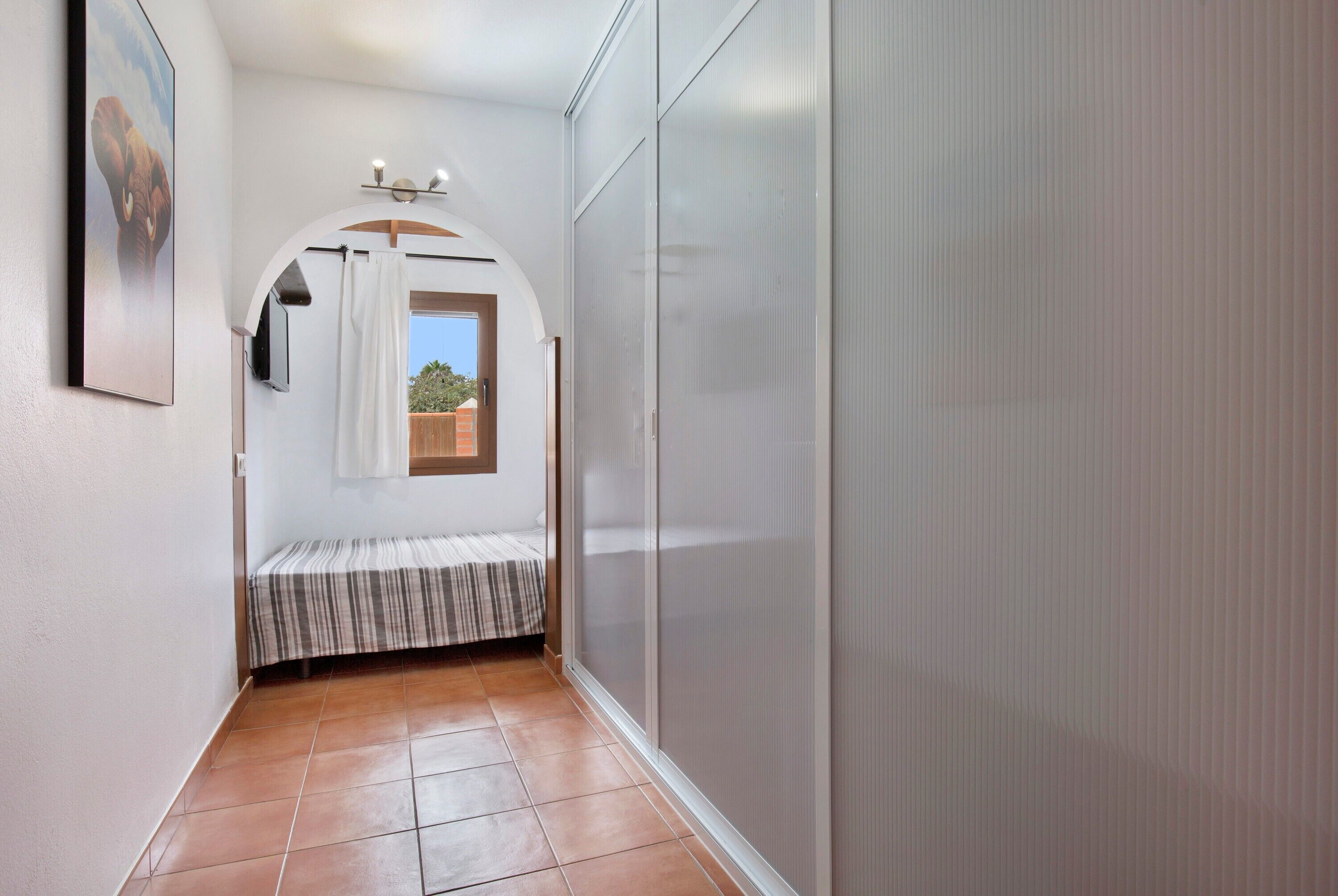 Un couloir étroit avec un lit, une fenêtre et une porte donnant sur un balcon.