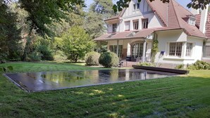 Una casa con una grande piscina, immersa in un prato curato e alberi.