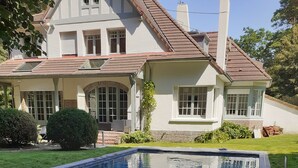 Una piscina con vista aperta sul paesaggio circostante, tra cui una casa con tetto in tegole e un prato curato.