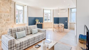 Un salon moderne avec un canapé à carreaux, une table à manger et un coin cuisine visible à travers une porte ouverte.