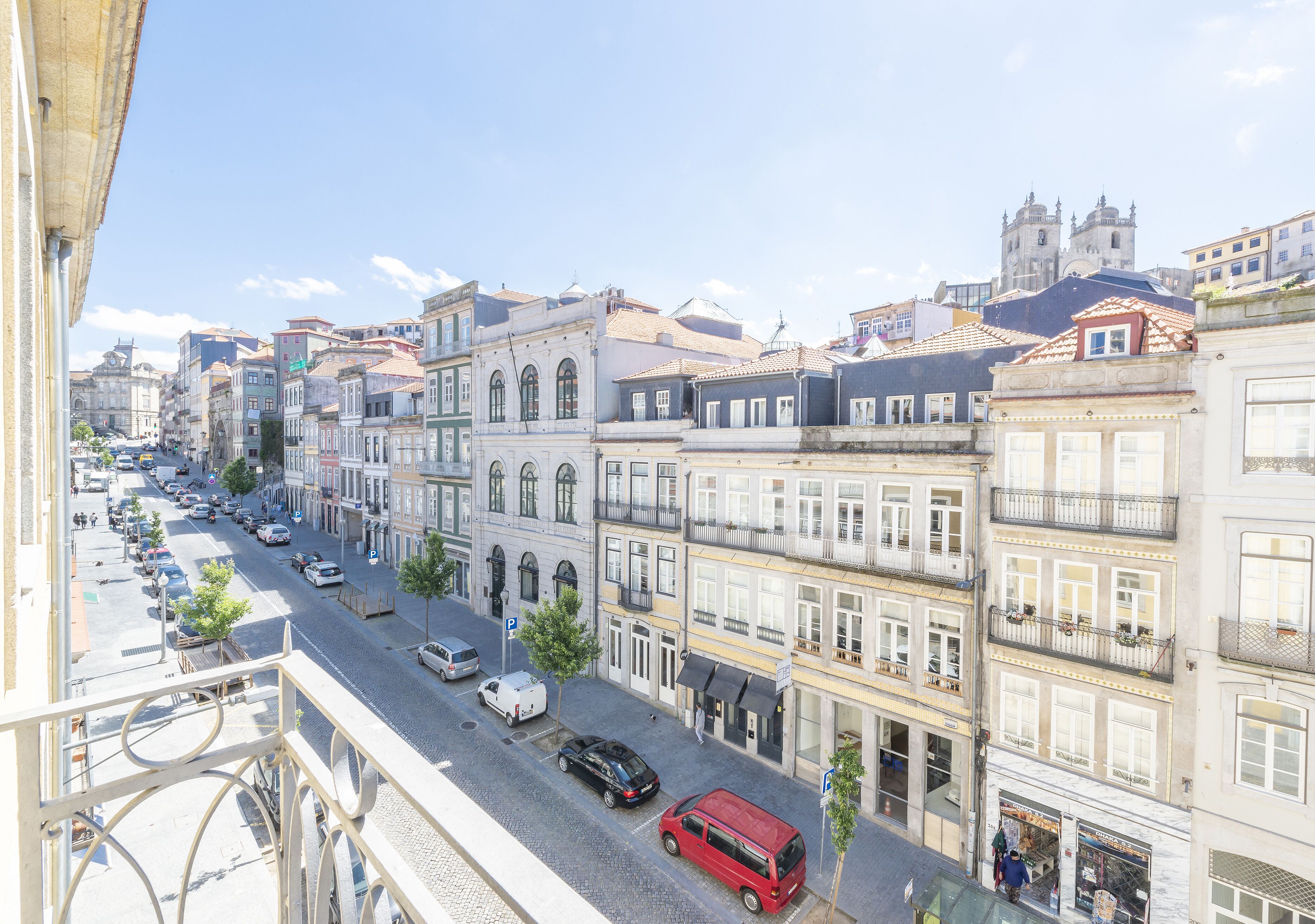 A street view with multi-story buildings, parked cars, and a clear sky.