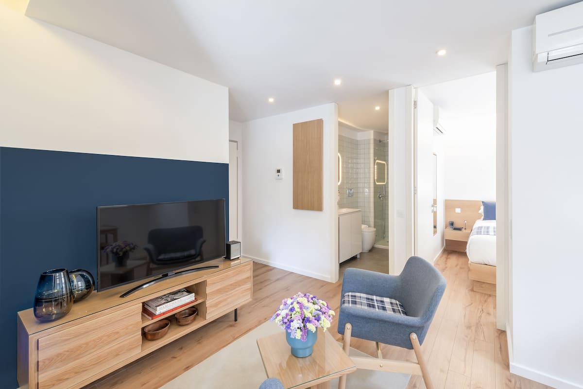 Un salon moderne avec un téléviseur à écran plat, un meuble de rangement en bois et un fauteuil bleu.