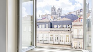 Une vue à travers une fenêtre sur un paysage urbain, avec des bâtiments historiques et un clocher d’église imposant.
