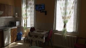 Cocina funcional con microondas, pileta y muebles bajos de madera. Se observa una mesa con sillas y un televisor montado en la pared.