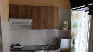 Cocina compacta con armarios de madera, lavavajillas blanco, microondas y cafetera en un estante.