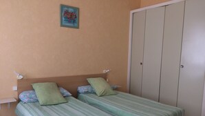 Un dormitorio con dos camas, cada una con ropa de cama verde a rayas, un cuadro pequeño en la pared y un armario.