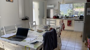 A modern kitchen with a dining area, featuring a laptop on the table, a refrigerator, and a window with a view of the outside. - le lac Devant sa Porte- Base de Bombannes Proche , Ocean à 5 Minutes (Carcans)