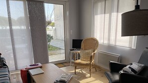 A living room with a wooden table, a wicker chair, a black sofa, and a television. - le lac Devant sa Porte- Base de Bombannes Proche , Ocean à 5 Minutes (Carcans)
