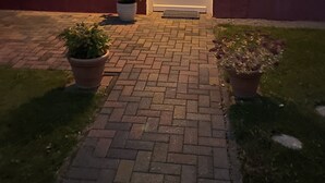 Un bâtiment rouge avec une porte blanche, des plantes en pot et un chemin de briques menant à l’entrée.
