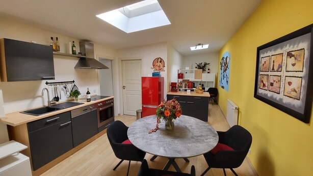 Une cuisine compacte dotée d’un puits de lumière, un coin repas avec une table ronde et un mur jaune vif agrémenté d’une œuvre d’art encadrée.