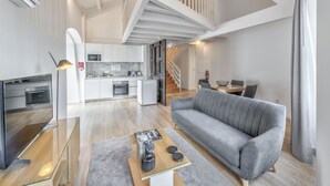 Ein modernes Wohnzimmer mit einem grauen Sofa, einem Glastisch und einem Flachbildfernseher.