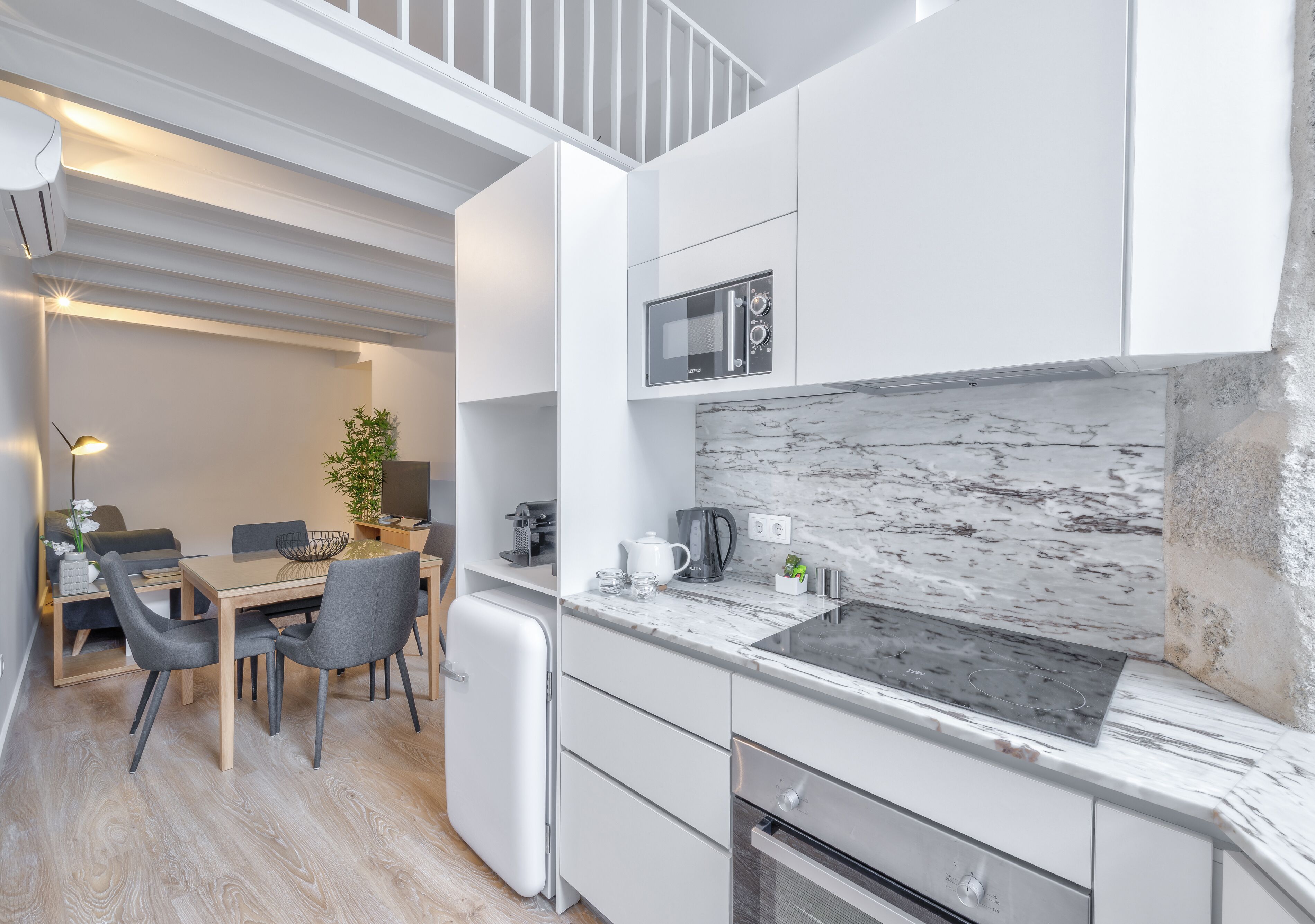 Una cocina moderna con armarios blancos, un salpicadero de mármol, un microondas integrado y un refrigerador pequeño.