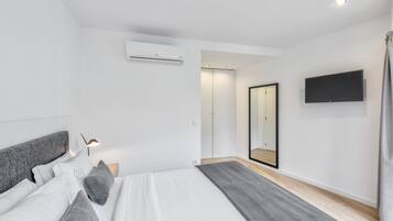 A modern bedroom with a bed, bedside table, lamp, air conditioning unit, wardrobe, mirror, and a TV mounted on the wall.
