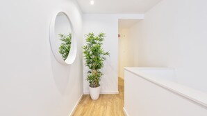 Ein Flur mit weißer Wand, einem runden Spiegel und einem Blumentopf.