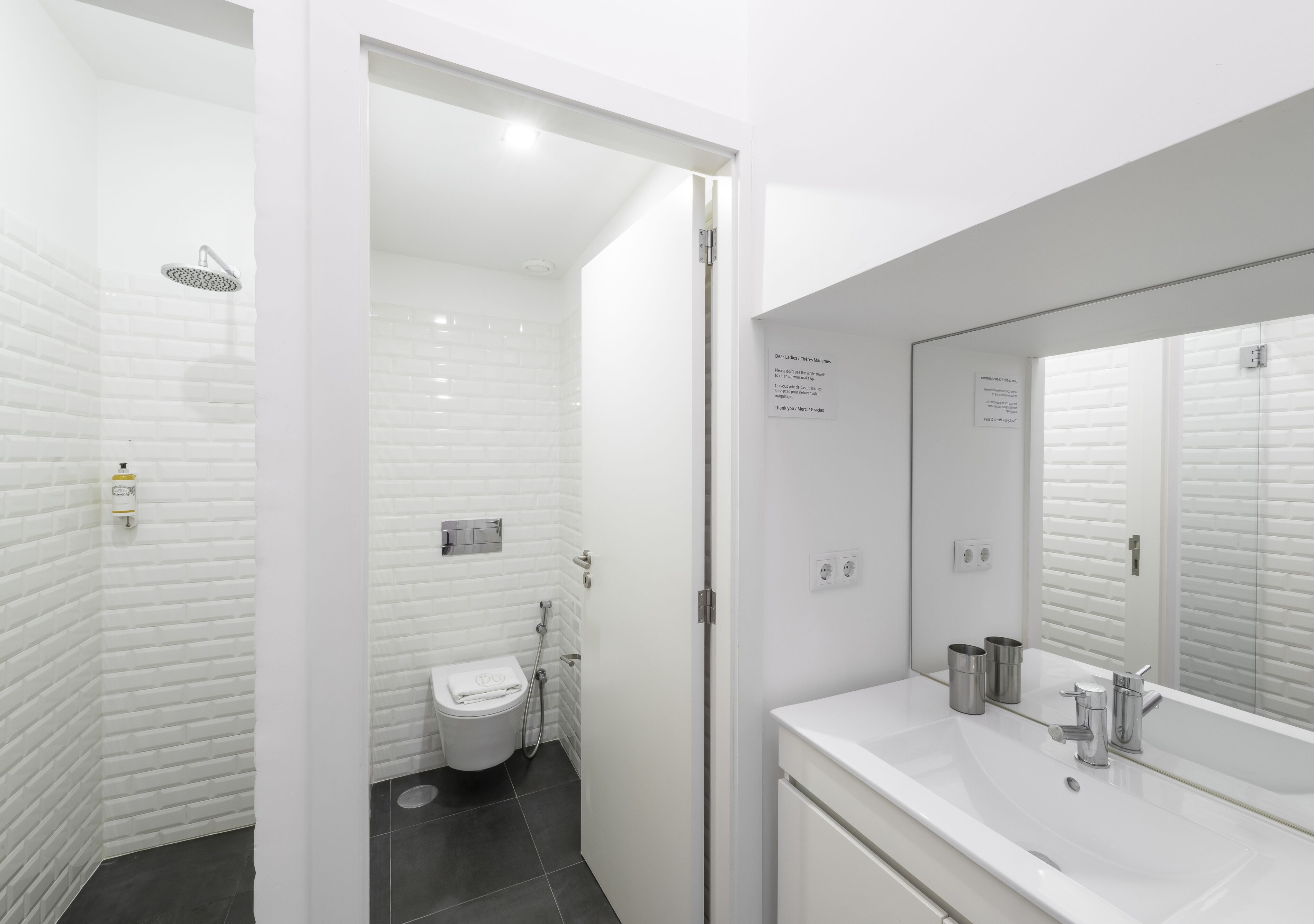 Un baño moderno con azulejos blancos tipo metro, inodoro blanco, ducha y un espejo grande sobre el lavamanos.