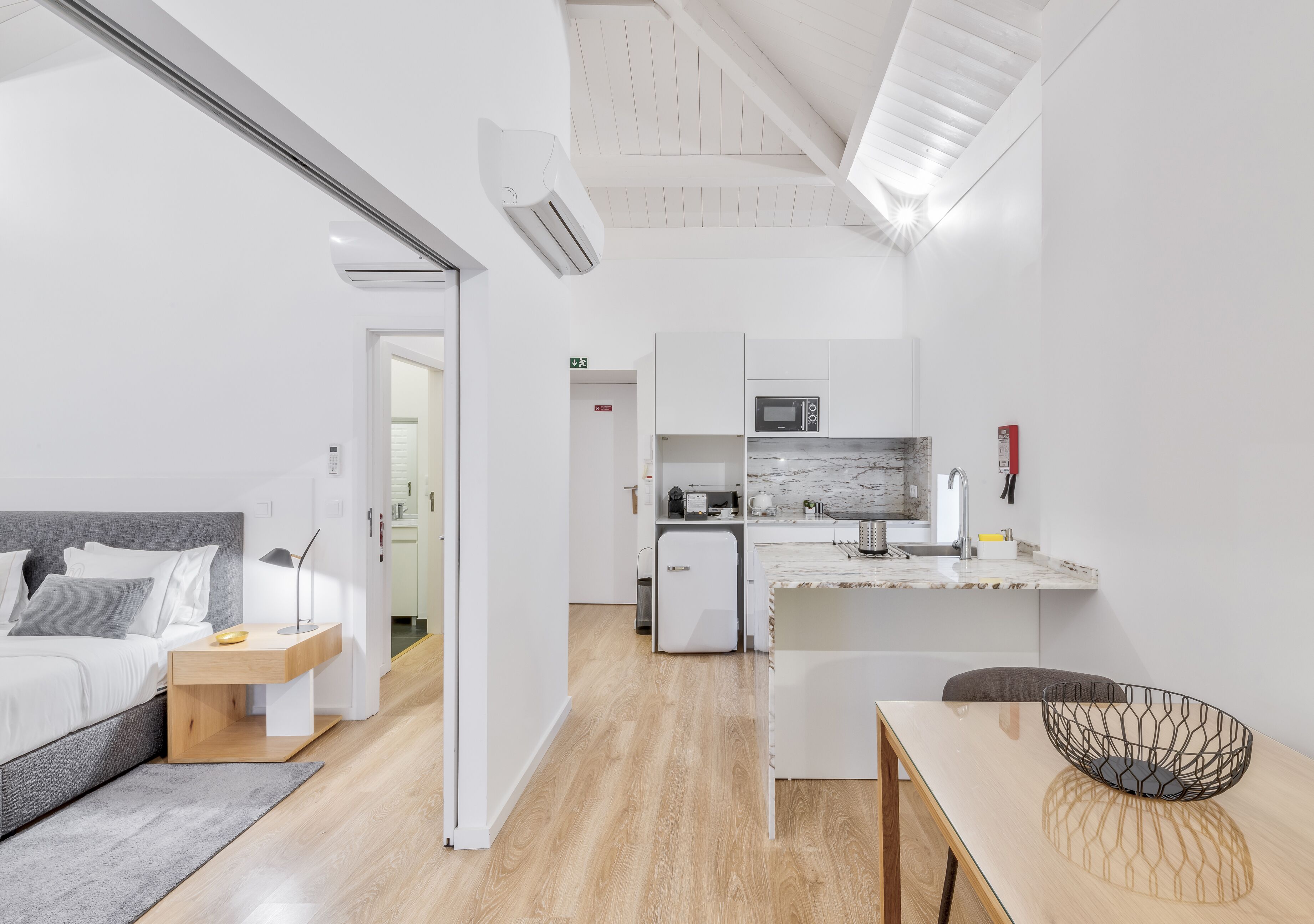 A modern, compact hotel room with a bed, bedside table, and a small kitchenette.