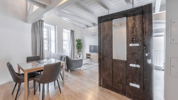 Ein moderner Essbereich mit Holztisch und -stühlen, einer Couch und einer großen Holztür.