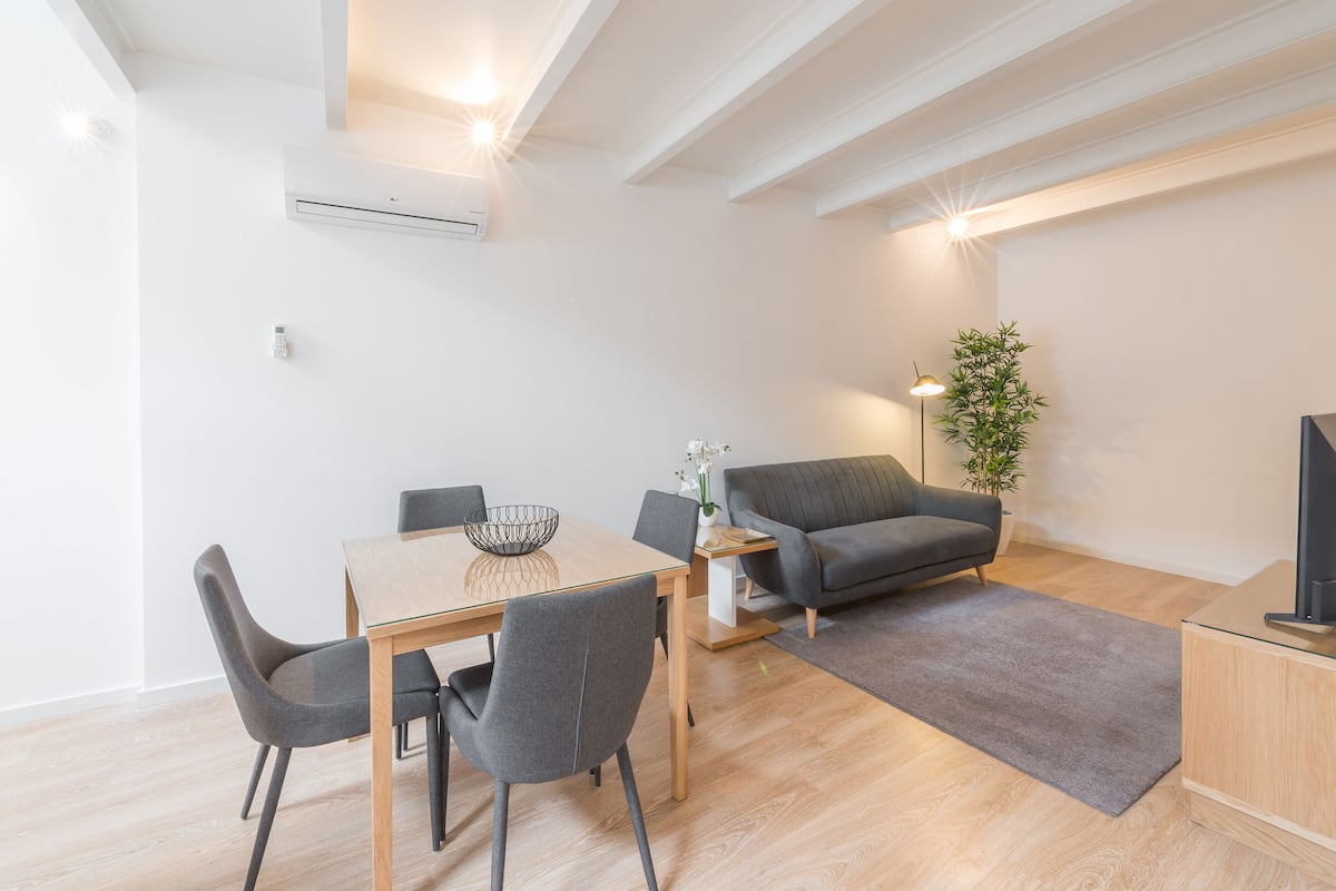 Un salon moderne avec une table à manger, des canapés gris et un téléviseur à écran plat.