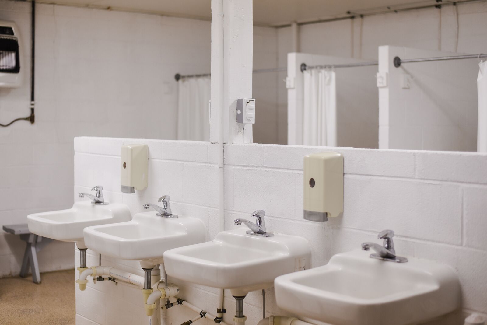 Ein Badezimmer mit vier weißen Waschbecken, jeweils mit Seifenspender, und einem großen Spiegel darüber.
