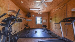 Ein Fitnessraum mit verschiedenen Trainingsgeräten, einem Deckenventilator und einem Fenster.