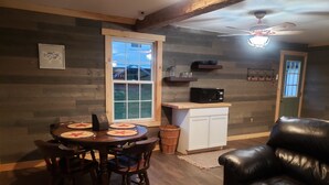 A cozy dining area with a wooden table and chairs, a white cabinet, and a black leather couch. - Charming one room cabin perfect for couples or small families. (Flat Rock)