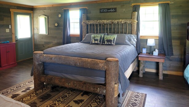 A rustic bedroom with a wooden bed, a red cabinet, and a 'STAY awhile' sign on the wall. - Charming one room cabin perfect for couples or small families. (Flat Rock)