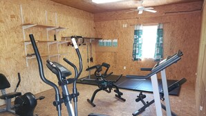 A gym with exercise equipment, a ceiling fan, and a window with curtains. - Charming one room cabin perfect for couples or small families. (Flat Rock)