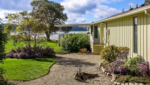 A house with a covered porch, a gravel pathway, and a garden with various plants. - Hood Canal Beach house, Low bank waterfront,  enjoy nature from your deck (Belfair)