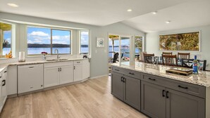 A modern kitchen with a large island, a view of the lake, and a dining area with a table and chairs. - Hood Canal Beach house, Low bank waterfront,  enjoy nature from your deck (Belfair)