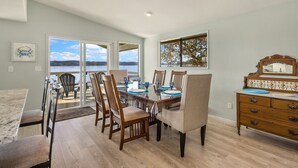 A dining area with a view of the lake, wooden chairs, a table set for four, and a dresser with a mirror. - Hood Canal Beach house, Low bank waterfront,  enjoy nature from your deck (Belfair)