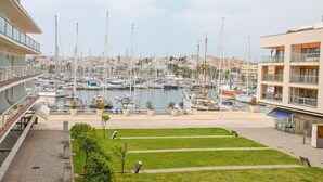 Una marina con numerose imbarcazioni ormeggiate, una zona erbosa in primo piano e edifici con balconi che si affacciano sulla marina.