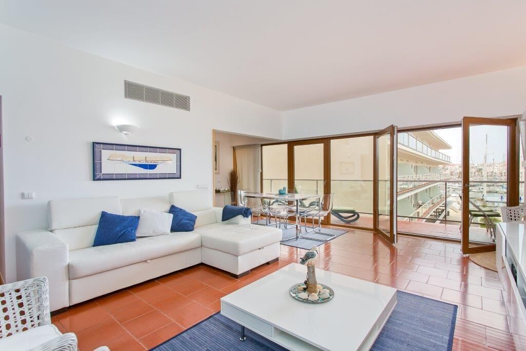 A modern living room with a white sofa, a coffee table, and a dining area with a glass table and chairs.