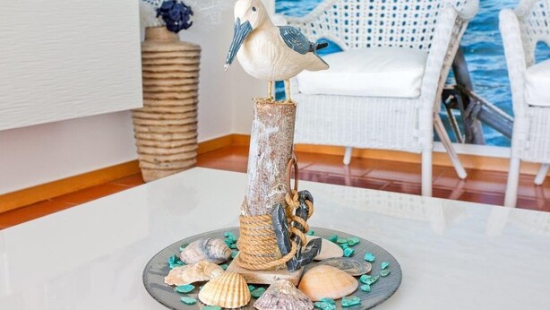 Una scultura di un uccello decorativo su una base rustica con conchiglie, posizionata su un tavolo in una stanza con una sedia bianca e una parete a tema oceano blu.
