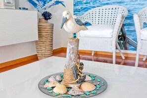 Eine dekorative Vogel-Skulptur auf einem rustikalen Sockel mit Meeresschnecken, platziert auf einem Tisch in einem Zimmer mit einem weißen Stuhl und einer Wand im blauen Meer-Design.