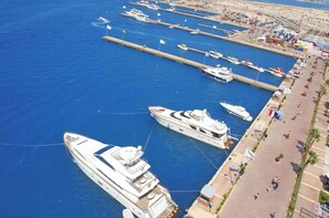 Ein Yachthafen mit mehreren Yachten an den Liegen, eine Promenade mit Menschen und ein Gebäude mit der Aufschrift 'STELLA' am Kai.