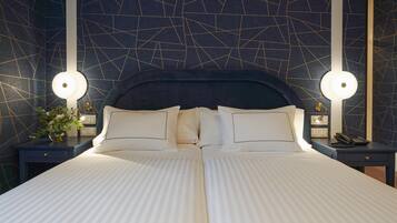Cama doble con ropa de cama blanca, dos mesitas de noche con lámparas y una pared con estampado geométrico.