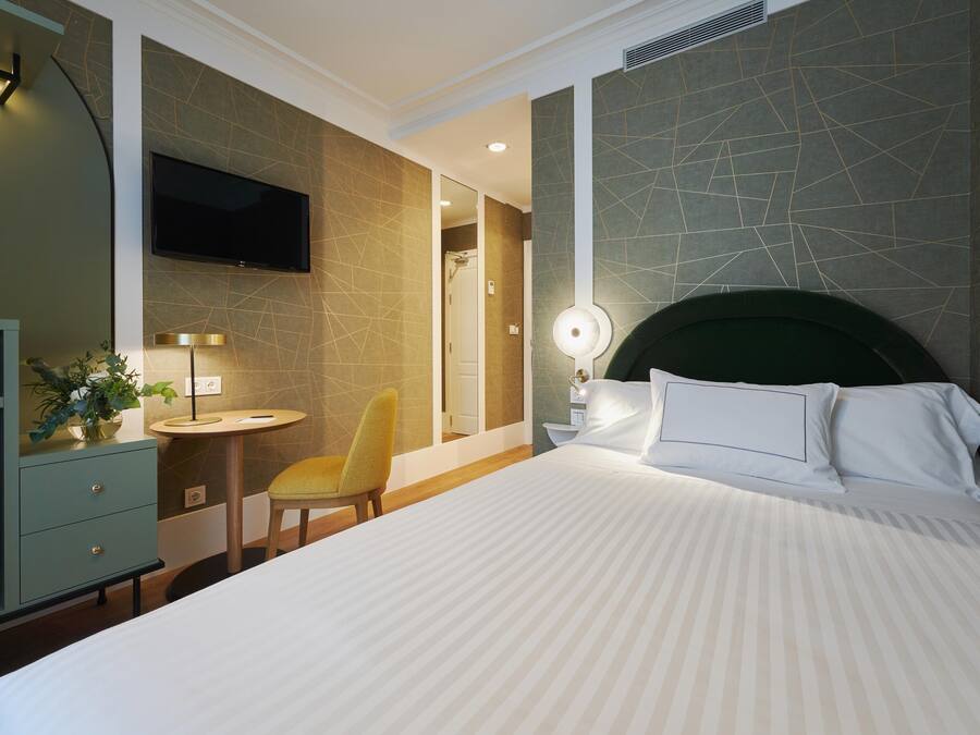 Una camera d'albergo con un letto, una scrivania, una sedia, una TV e un bagno visibile attraverso una porta aperta.